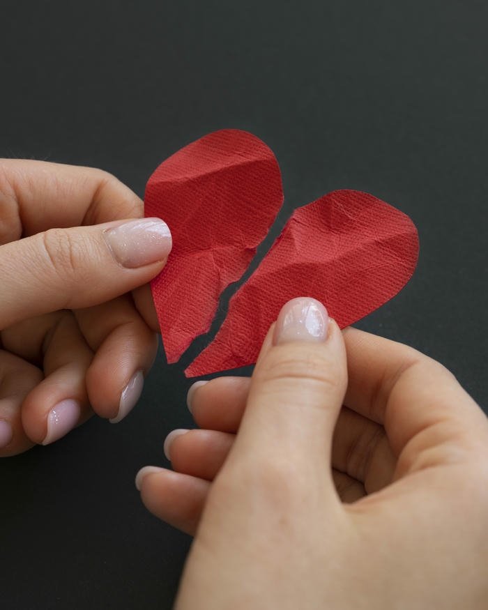 Broken heart hands holding two red pieces apart on wood
