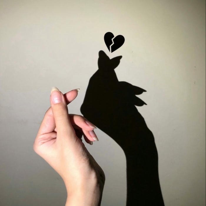 Hand shadow art forming a broken heart on wall