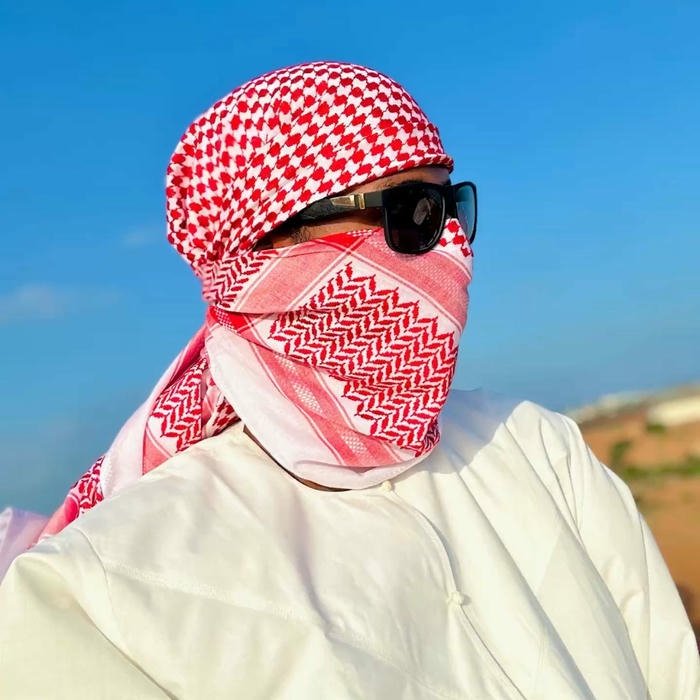 Man covering face with red scarf against blue sky